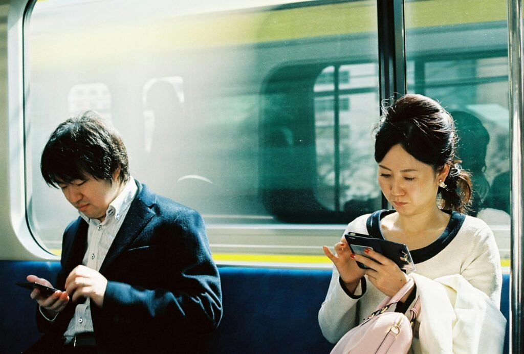 Useful Japanese Etiquette for Tourists: Essential Tips Before You Visit 5 Two people using smartphones on a train in Tokyo, Japan. Captures daily commute and technology use.